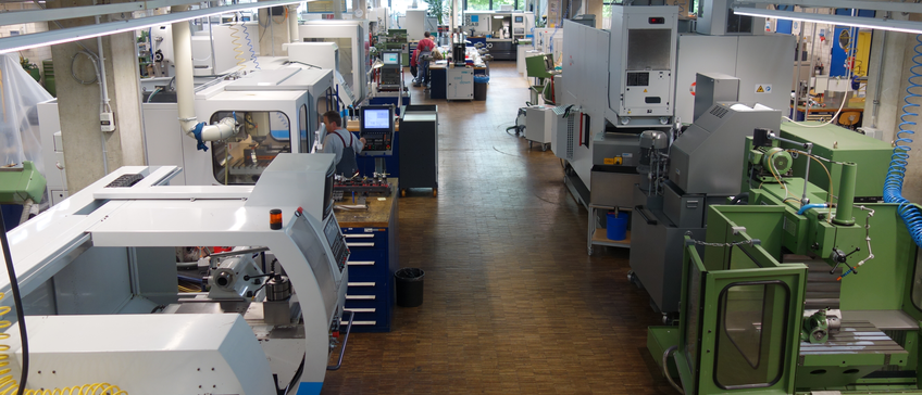 Apprenticeship program Spacious factory floor of our mechanical workshop featuring modern machinery, including CNC machines and workstations, with workers attending to different manufacturing tasks.