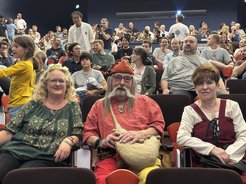 Gefüllter Hörsaal, mit drei Personen in mittelalterlichen Kostümen im Vodergrund.